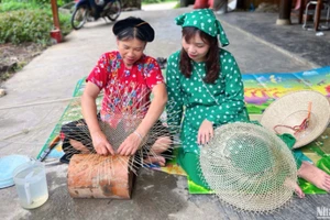 Madame Hoang Thi Hue (à gauche) échange avec des visiteurs et leur montre comment confectionner un chapeau.