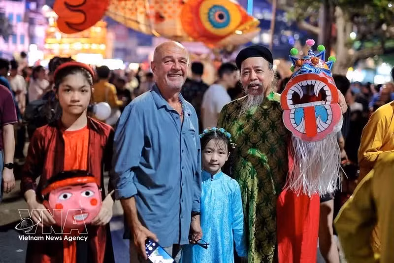 Des touristes internationaux s'imprègnent de l'ambiance de la Fête de la mi-automne au bord du lac Hoan Kiem, entourés de jouets traditionnels colorés. Photo : VNA.
