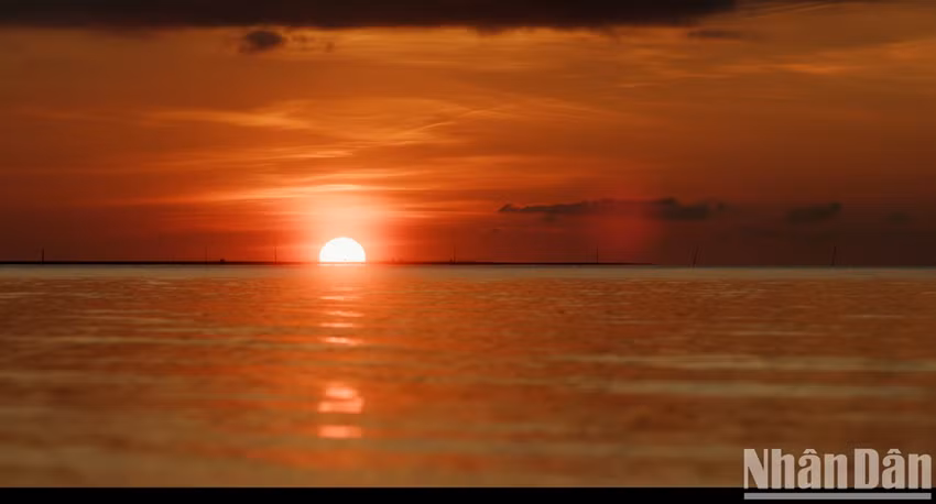La surface de la mer scintille de reflets roses et orangés, miroir éclatant des couleurs vives du ciel, composant un paysage féerique que nul témoin ne pourrait jamais oublier. Photo : Nhân Dân.