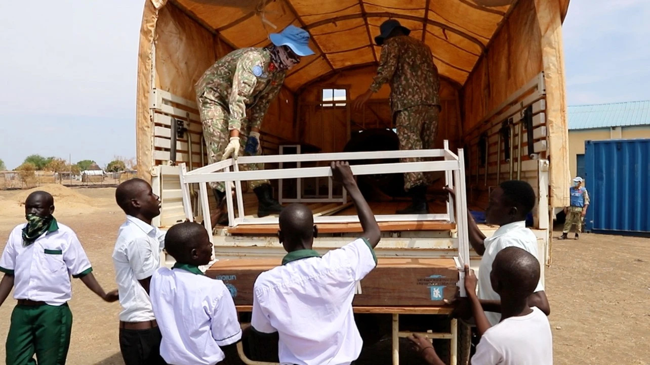 Le personnel de la 2e sous-unité de construction du génie militaire n° 3 et les élèves de l'école d'Abyei déchargent et transportent les tables-bancs offerts.