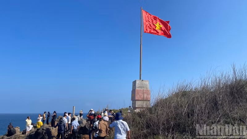 Des visiteurs prennent des photos près du mât de drapeau.