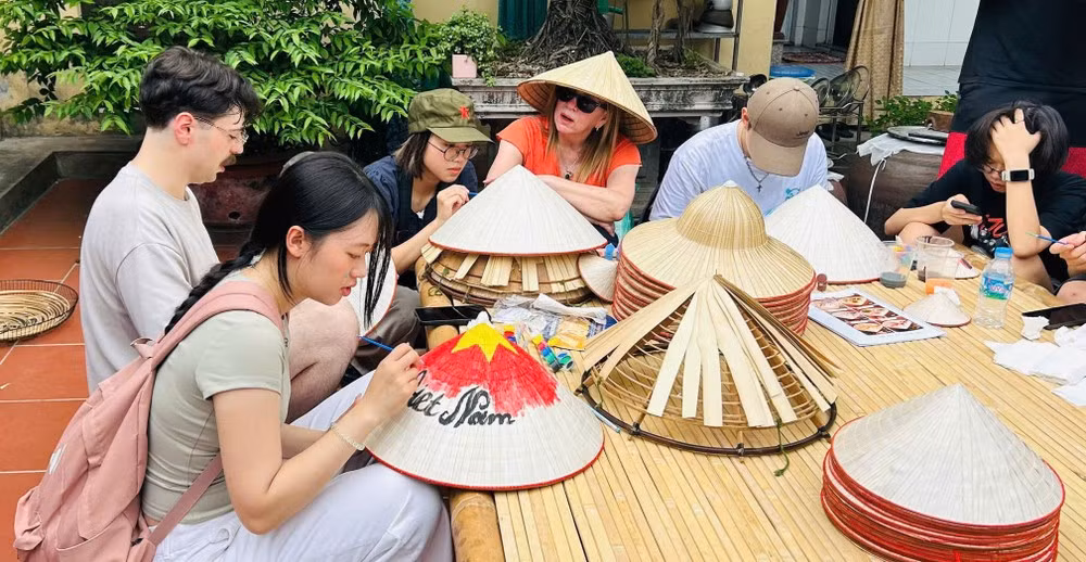Des touristes s'essaient à la fabrication des chapeaux coniques Tri Le dans la commune de Dan Hoa. Photo : TRILAF
