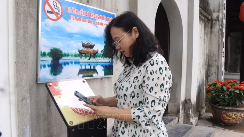 Des visiteurs scannent un code QR pour découvrir le parcours de visite numérisé au site historique du temple Do. Photo : VNA.
