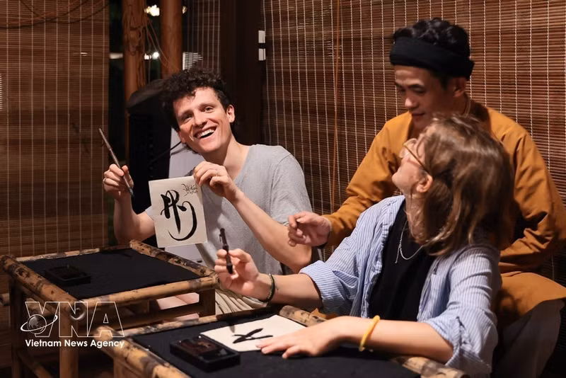 Des touristes étrangers découvrent l'art de la calligraphie au Temple de la Littérature. Photo : VNA.