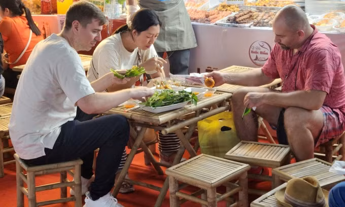 Thomas (chemise rose) déguste du banh can trempé dans une sauce de poisson aigre-douce lors du festival le soir du 23 octobre. Photo : Bich Phuong.