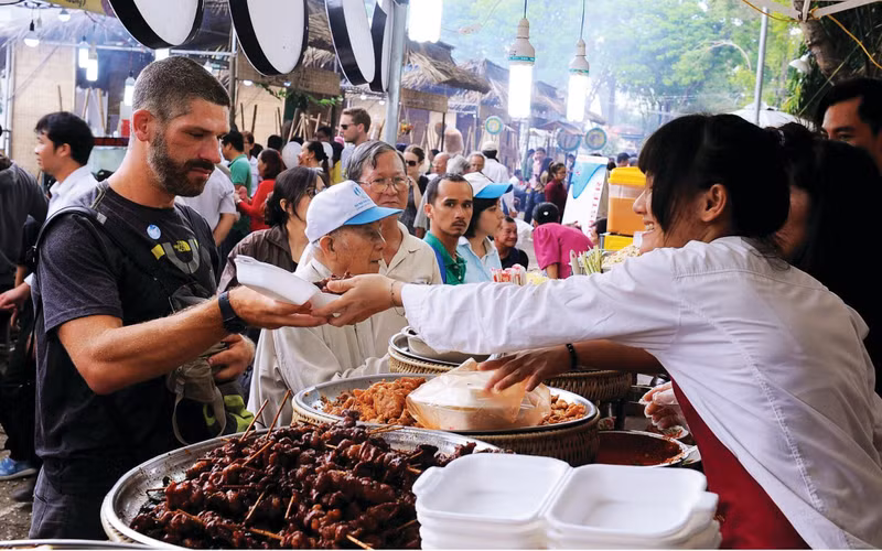 Un touriste étranger (gauche) découvre la cuisine de rue à Hanoï.
