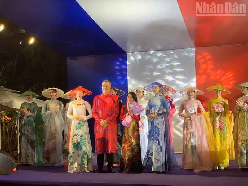L'ambassadeur Olivier Brochet offre des fleurs pour féliciter la créatrice et la collection d'ao dai présentée lors de l'événement. Photo : NDEL