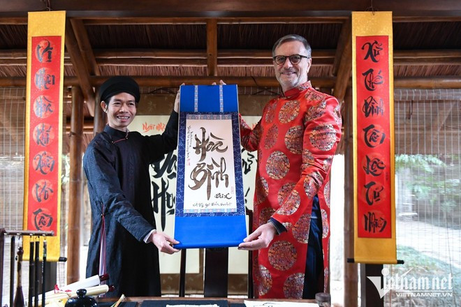 L’ambassadeur Olivier Brochet s’est initié à la calligraphie avec l’aide d’un lettré et s'est vu offrir un tableau portant l'inscription «Paix ». Photo : Vietnamnet.