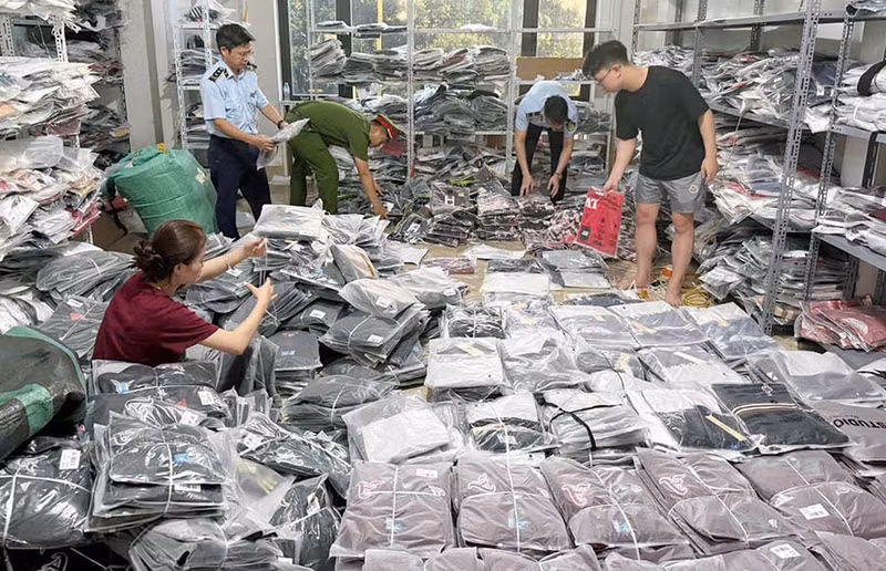 Des agents compétents inspectent des produits contrefaisant des marques célèbres dans un établissement de vente de vêtements de la zone industrielle de Ninh Hiep (commune de Phu Dong). Photo : Hanoimoi.