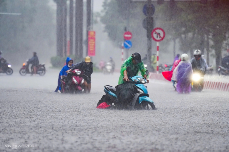 Des habitants poussent leurs motos dans la rue Nguyen Hoang, submergée par les inondations. Photo : VnExpress.