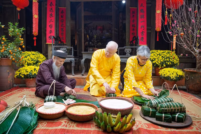 Des touristes étrangers découvrent la préparation du bánh chưng dans l'ancien village de Duong Lâm. Photo : Nina May. Des touristes étrangers découvrent la préparation du bánh chưng dans l'ancien village de Duong Lâm. Photo : Nina May.
