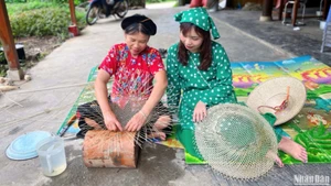 Madame Hoang Thi Hue (à gauche) échange avec des visiteurs et leur montre comment confectionner un chapeau.