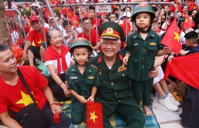 Un vétéran et ses enfants arrivent tôt à l'intersection Hung Vuong-Tran Phu pour assister à la deuxième répétition générale du défilé. Photo : Van Diep - VNA Un vétéran et ses enfants arrivent tôt à l'intersection Hung Vuong-Tran Phu pour assister à la deuxième répétition générale du défilé. Photo : Van Diep - VNA
