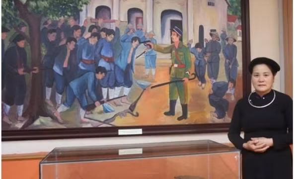 La guide Nông Thi Bich se tient à côté du tableau représentant la bataille de Phai Khat et des artefacts historiques de cette bataille. Photo : VOV.