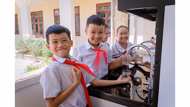 Les enfants sont contents de boire de l'eau propre provenant du système de traitement de l'eau potable financé par la Fondation Lifestart. Photo : baoquangnam.vn