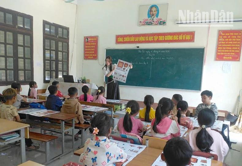 Une enseignante de l'école primaire Ngoc Chien dans le district de Muong La, explique aux élèves comment découper et assembler une maquette de la Tour de drapeau de Hanoï tirée d'une publication spéciale du journal Nhân Dân. Photo : NDEL.