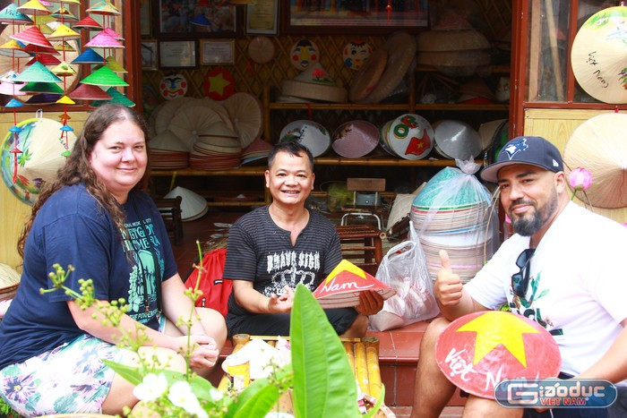 Le couple Aren et l'artisan Lê Văn Tuy posent pour une photo souvenir avec le chapeau que le couple a fini de colorier. Photo : Manh Doan Le couple Aren et l'artisan Lê Văn Tuy posent pour une photo souvenir avec le chapeau que le couple a fini de colorier. Photo : Manh Doan