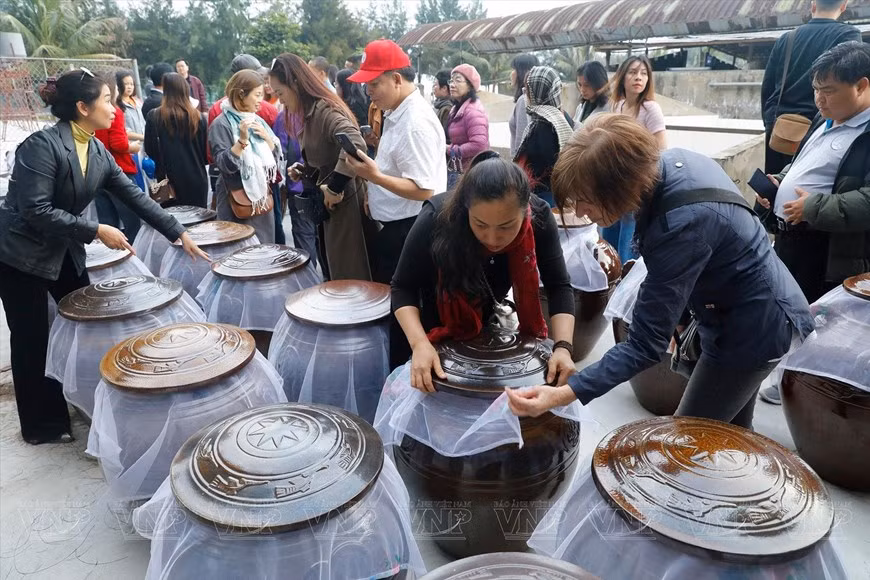 Des touristes visitent un établissement de production de sauce aux palourdes de Côn Den.