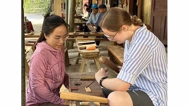 Les touristes aiment pouvoir essayer de sculpter du bois pour créer leurs propres produits avec les conseils des artisans du village. Photo : VOV.