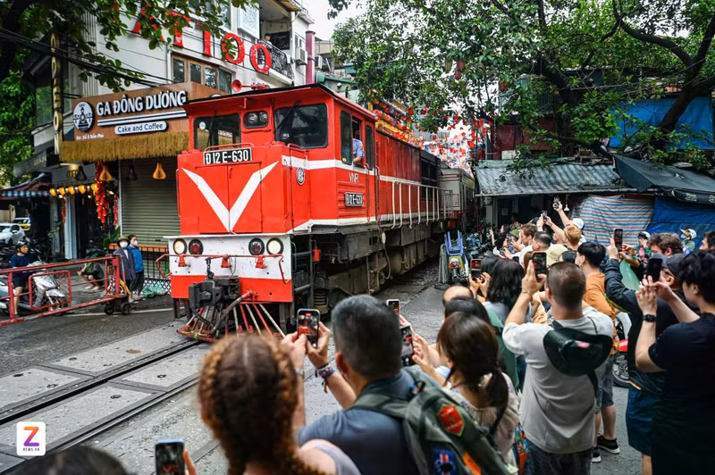 Des touristes étrangers s’enthousiasment en voyant un train passer au plus près d’une petite rue de Hanoï, en juillet 2025. Photo : znews.vn