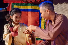 Une jeune s’initie à un instrument de musique auprès d'un artisan. Photo : VNA. 