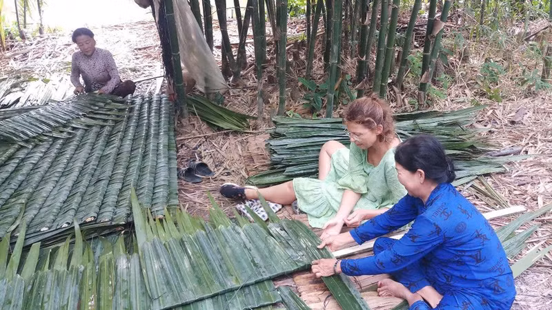 Des touristes apprennent à tisser des feuilles de palmier pour la toiture. Photo : baovanhoa.vn