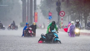 Des habitants poussent leurs motos dans la rue Nguyen Hoang, submergée par les inondations. Photo : VnExpress.