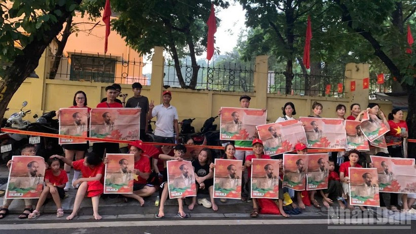 Les citoyens brandissent le supplément du journal Nhân Dân illustré par une photo de l’oncle Hô accueillant le cortège militaire sur la rue Cua Bac.