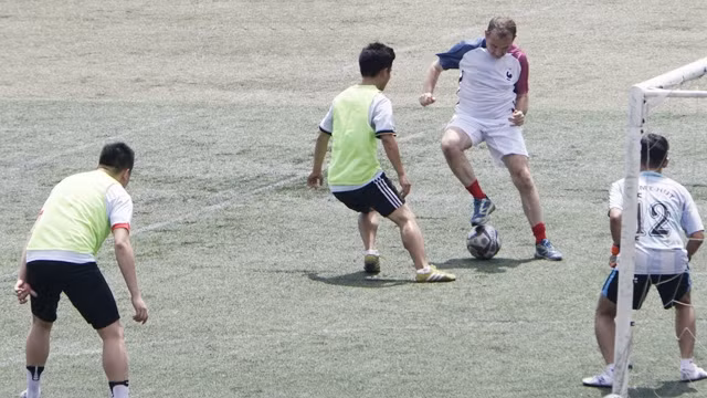 L’ambassadeur de France (maillot tricolore) joue au football.