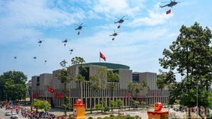 Une formation de dix hélicoptères arborant le drapeau du Parti et le drapeau national survolent la place Ba Dinh. Photo : Giang Huy.