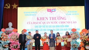 La vice-ambassadrice de la République démocratique populaire lao au Vietnam, Lattana Sihalat (cinquième en partant de la gauche), remet des certificats de mérite aux collectifs et aux familles exemplaires pour leur engagement à accueillir des étudiants laotiens comme enfants adoptifs. Photo : thoidai.com.vn