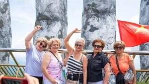 Les touristes étrangers apprécient de se prendre en photo sur le pont d’Or, orné de drapeaux vietnamiens éclatants, dans la zone touristique. Photo : baoquocte.vn