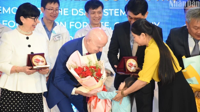 Une petite patiente remet des fleurs en signe de gratitude au professeur Erich Johann Lejeune. Dans quelques jours, elle bénéficiera d’une opération cardiaque prise en charge par l’organisation "Heart for Heart".Photo : Nhân Dân.