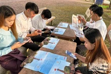 Des étudiants lao à Son La font l'expérience de la technologie numérique en scannant les codes QR pour en savoir plus sur le Jour de la libération de la capitale Hanoi dans la publication spéciale « la Tour du drapeau de Hanoi » du journal Nhân Dân. Photo : NDEL.