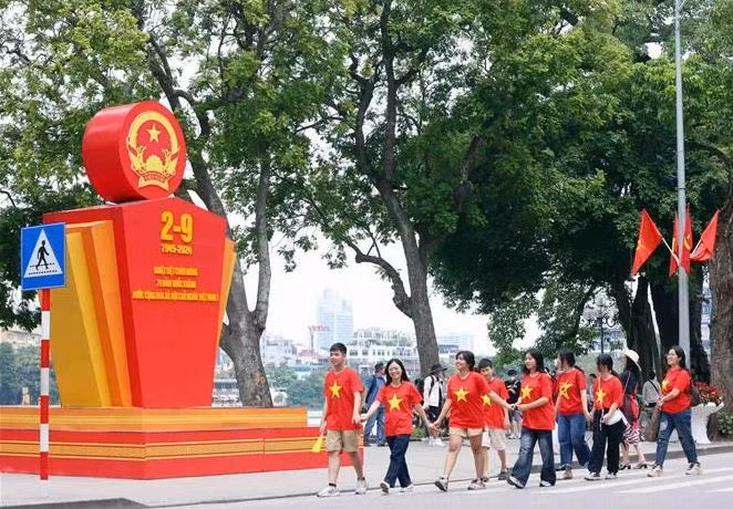 Des jeunes marchent en liesse devant un paneau célébrant la 79e Fête nationale du Vietnam, près du lac Hoàn Kiêm, à Hanoi. Photo : VNA.