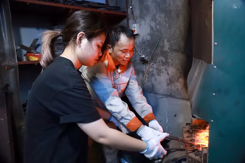 L'artisan Le Ngoc Lam guide avec enthousiasme une jeune pour fabriquer un couteau à la façon traditionnelle. Photo : baovanhoa.