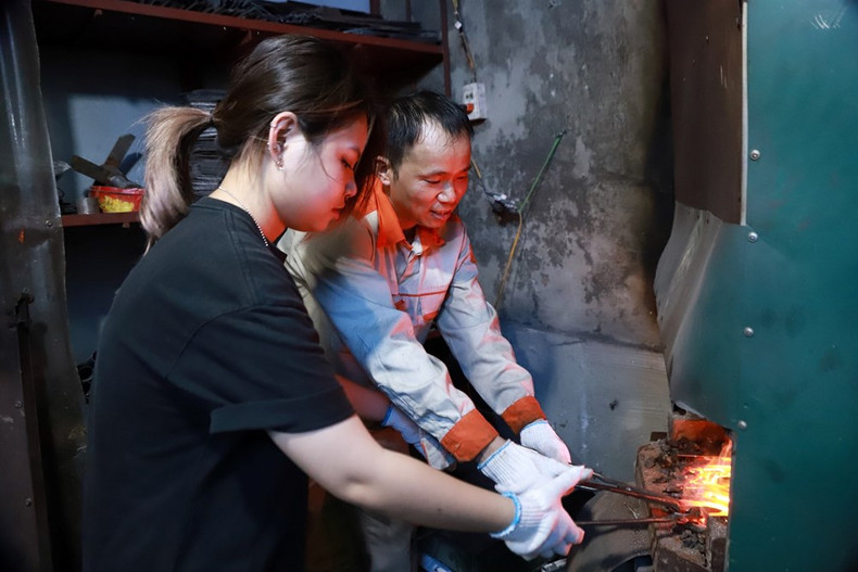 L'artisan Le Ngoc Lam guide avec enthousiasme une jeune pour fabriquer un couteau à la façon traditionnelle. Photo : baovanhoa.