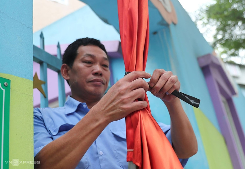 Un agent de sécurité d'une école maternelle de la rue Hai Ba Trung a utilisé un ruban noir pour attacher une partie du drapeau national avant de l'accrocher à la porte. Un agent de sécurité d'une école maternelle de la rue Hai Ba Trung a utilisé un ruban noir pour attacher une partie du drapeau national avant de l'accrocher à la porte.