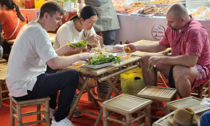 Thomas (chemise rose) déguste du banh can trempé dans une sauce de poisson aigre-douce lors du festival le soir du 23 octobre. Photo : Bich Phuong. Thomas (chemise rose) déguste du banh can trempé dans une sauce de poisson aigre-douce lors du festival le soir du 23 octobre. Photo : Bich Phuong.