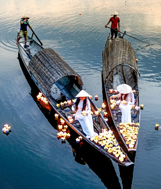Deux femmes portant des non la (chapeau conique) et des ao dai (tenue traditionnelle vietnamienne) libèrent des lampions depuis deux bateaux en bois sur la rivière Nhu Y à Hue. Photo de Nguyen Minh Tuan publiée dans la rubrique Travel de CGTN.