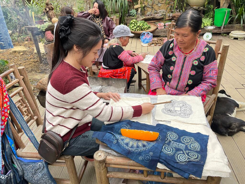 Une visiteuse pratique la technique du batik (dessin à la cire d’abeille sur tissu) sous le guidage d'une femme H'mông. Photo : CVN