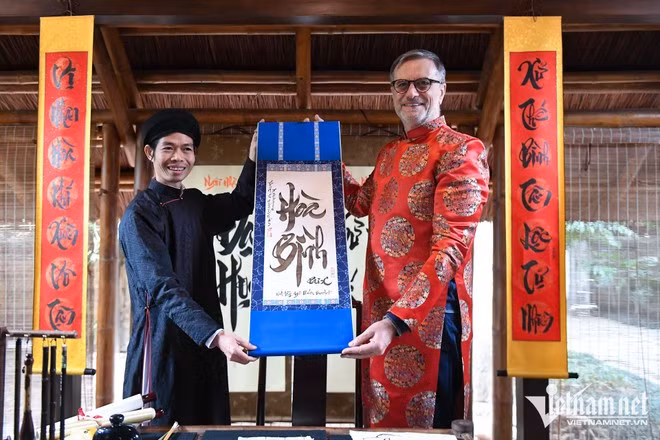 L’ambassadeur Olivier Brochet s’est initié à la calligraphie avec l’aide d’un lettré et s'est vu offrir un tableau portant l'inscription «Paix ». Photo : Vietnamnet.