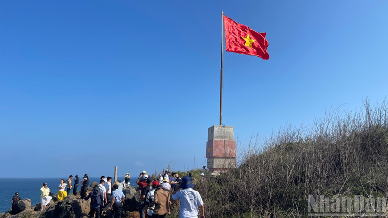 Des visiteurs prennent des photos près du mât de drapeau.