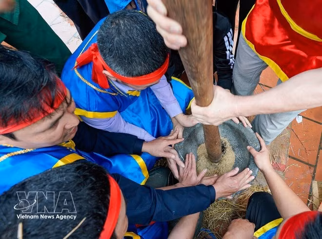 Les jeunes hommes des équipes pilent le paddy dans un mortier en pierre. Photo : VNA.