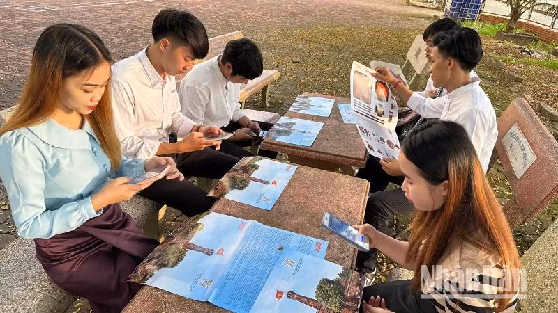 Des étudiants lao à Son La font l'expérience de la technologie numérique en scannant les codes QR pour en savoir plus sur le Jour de la libération de la capitale Hanoi dans la publication spéciale « la Tour du drapeau de Hanoi » du journal Nhân Dân. Photo : NDEL.