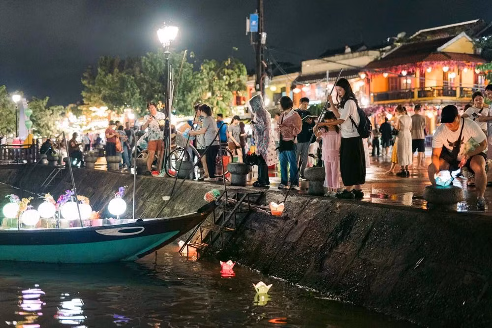 À la tombée de la nuit, des visiteurs déposent des lanternes flottantes sur la rivière Hoai.