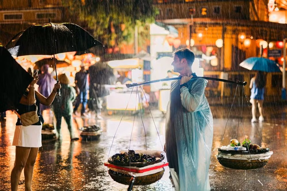 Sous une pluie battante, des visiteurs étrangers s’amusent à porter la palanche d’une vendeuse ambulante.