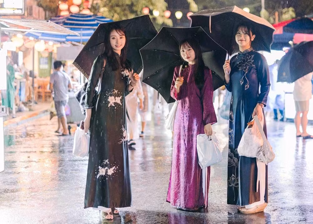 Trois touristes japonaises vêtues de l’áo dài se promènent sous la pluie dans les rues de Hoi An.
