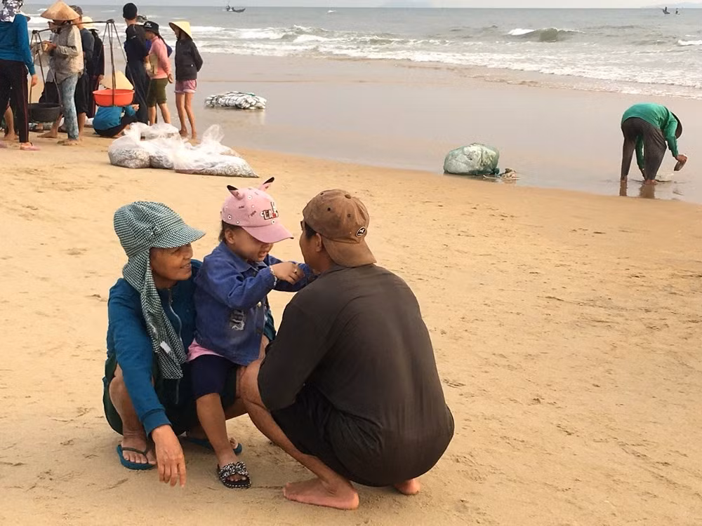 Un moment de calme au milieu du marché : les adultes discutent tandis qu’un enfant accueille avec joie son père de retour d’une nuit en mer. À l’arrière-plan, les transactions se poursuivent. Photo : VHO.
