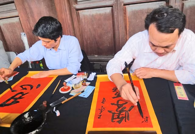 Les lettrés calligraphes écrivent les idéogrammes chinois sur les papiers pourpres avec la plume et l'encre de Chine. Photo: Minh Hanh/NDEL.